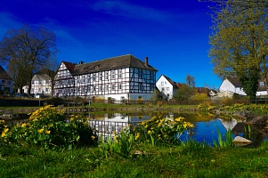 Zu sehen ist ein großes Fachwerkgebäude in Ottenstein, welches heute die Landherberge beherbergt.  Davor ist der Dorfteich zu sehen, dieser ist umgeben von gelben Blumen. Rechts hinter dem Fachwerkgebäude sind weitere Häuser zu sehen. Der Himmel ist blau. Das Gebäude spiegelt sich im Wasser des Teiches.&nbsp;&copy;&nbsp;Samtgemeinde Bodenwerder-Polle/Rolf Sander