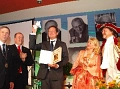Dr. Eckart von Hirschhausen steht mittig, während er lächelnd den Münchhausenpreis in die Höhe und vor sich sein Buch geöffnet hält. Links neben ihm steht unter anderem der Bürgermeister von Bodenwerder und rechts der Baron von Münchhausen mit Ehefrau. Er&nbsp;&copy;&nbsp;Frank Neitz