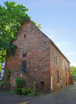 Zu sehen ist das Gebäude der Gertrudis-Kapelle, welches aus Weser-Sandstein gebaut wurde. Hier zu sehen ist der ehemalige Eingang über eine Treppe und eine dunkle Holztür an der Seite des Gebäudes. An der langen Seite des Gebäudes ist der neue Treppenaufgang zu sehen.&nbsp;&copy;&nbsp;Samtgemeinde Bodenwerder-Polle/LeoDesign
