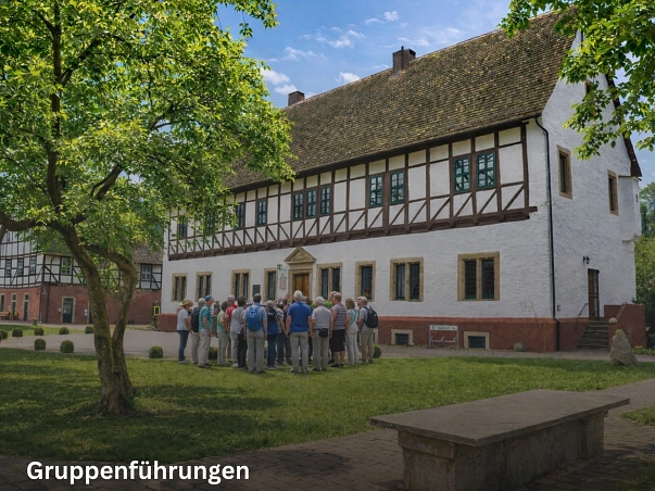 Gruppenführungen.jpg Zu sehen ist das heutige Rathaus in Bodenwerder, ein weißes Fachwerkgebäude mit sandsteinfarbenem Sockel. Vorne rechts im Vordergrund steht ein Steintisch. Hinten links im Hintergrund ist das ehemalige Brennereihaus und heutige Verwaltungsgebäude zu sehen. Dies hat ebenfalls einen sandsteinfarbenen Sockel und ein Obergeschoss aus Fachwerk. Vor dem Rathaus ist eine Grünfläche sowie ein Baum. Direkt vor dem Rathaus steht einen Personengruppe während einer Stadtführung. © Samtgemeinde Bodenwerder-Polle/bearbeitet mit KI