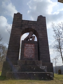 Zu sehen ist das Herzog-Wilhelm-Denkmal auf dem Rühler Weinberg bei Rühle. Es ist ein Torbogen aus Stein und im Durchgang steht ein die Inschrift "Wilhelm Herzog zu Braunschweig und Lüneburg, geboren 25. April 1806, gestorben 18. Oktober 1884. Seinem Andenken in treuer Dankbarkeit gewidmet. 17. Juni 1909.". Darauf sitzt ein Löwe, welcher in die Ferne schaut und mit seiner Pfote ein Wappen mit einem Pferd hält.&nbsp;&copy;&nbsp;Samtgemeinde Bodenwerder-Polle