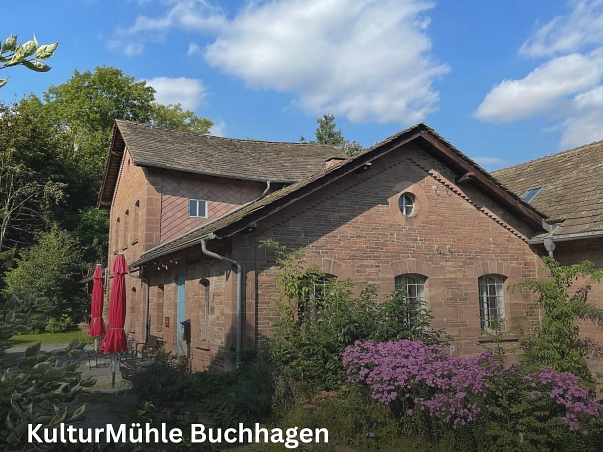 KulturMühle Buchhagen.jpg Auf dem Bild ist die KulturMühle sowie das dazugehörige MühlenCafé in Buchhagen zu sehen. Die historische Sandsteinmühle wurde 1867 erbaut, seit 1908 ist der Schleifbetrieb eingestellt. Links vor dem Gebäude stehen zwei zusammengeklappte rote Sonnenschirme sowie ein paar Stühle mit Tisch. Im Vordergrund sind einige grüne Büsche und Bäume zu sehen sowie auf der rechten Seite lila blühende Blumen. © Samtgemeinde Bodenweder-Polle/Simone Kelly