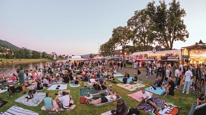 Das Bild zeigt die Weserpromenade in Bodenwerder am Tag des Lichterfestes 2025. Hier zu sehen sind auf der rechten Seite sowie bis in den Hintergrund verschiedene Verpflegungsstände, links ist die Weser zu sehen. Auf der Rasenfläche sitzen und liegen viele Menschen auf Decken oder auf dem Rasen. Auf dem Weg rechts sind ebenfalls viele Menschen zu Fuuß unterwegs.&nbsp;&copy;&nbsp;Purple Box Production GmbH