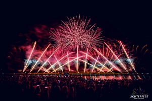Auf dem Bild ist das Ostufer der Weserpromenade in Bodenwerder aus Sicht der gegenüberliegenden Seite in der Dunkelheit zu sehen. Am Ostufer ist ein Feuerwerk in verschiedenen Pinktönen zu sehen. Das verschiedene Feuerwerk geht gerade sowie schräg in die Luft. Oben Mittig zerspringt gerade ein Feuerwerkskörper, sodass ein pinker Feuerwerks-Ball zu sehen ist.&nbsp;&copy;&nbsp;Purple Box Production GmbH