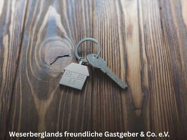 Weserberglands freundlichen Gastgeber & Co. e.V..jpg Zu sehen ist eine Oberfläche aus dunklem gemusterten Holz. Darauf liegt ein Schlüssel, der zusammen mit einem kleinen silbernen Anhänger, der ein haus darstellt, an einem Schlüsselring hängt. © Freepik