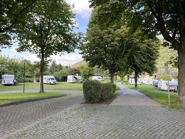 Wohnmobilstellplatz Bodenwerder Auf dem Bild ist auf der linken Seite der Teil des Stellplatzes zu sehen, auf dem Stromanschlüsse zur für die Wohnmobile Verfügung stehen und es einen befestigten Boden gibt.
Auf der rechten Seite des Bildes sind rechts vom Weg die direkt an der Weser liegenden Stellplätze auf einer Rasenoberfläche. Im Hintergrund ist die Eisenbahnbrücke zu sehen. © Samtgemeinde Bodenwerder-Polle